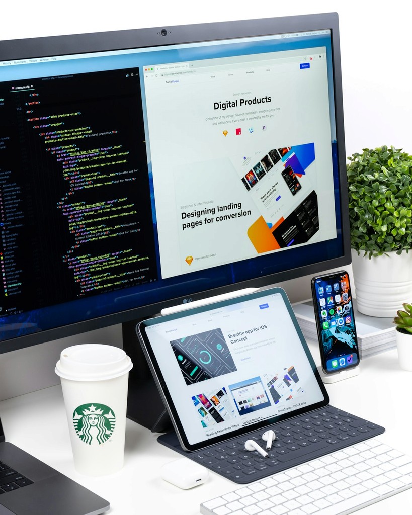 Poste de travail avec écran affichant du code et un site web en développement, tablette et smartphone posés sur un bureau moderne avec café