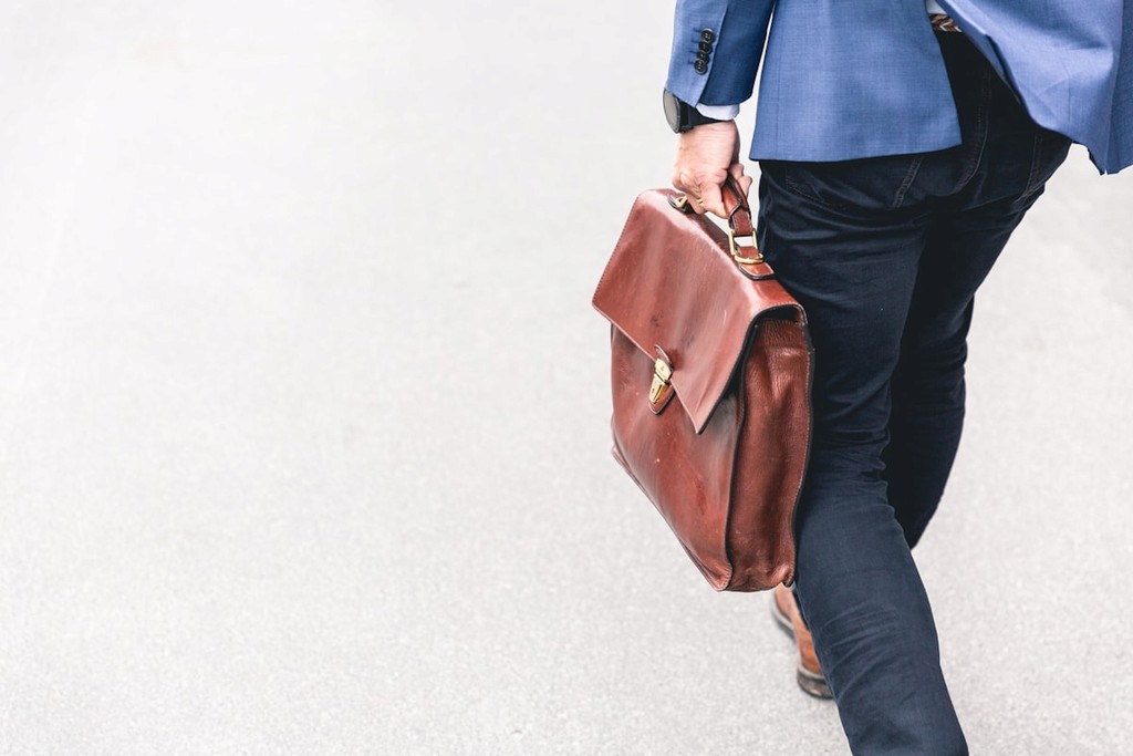 Homme d’affaires marchant avec une mallette en cuir, représentant le professionnalisme et les services corporatifs.